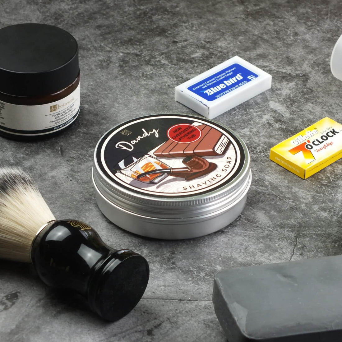 close up shot of our handmade Dandy shaving soap on a marbled surface with other shaving kit items next to it